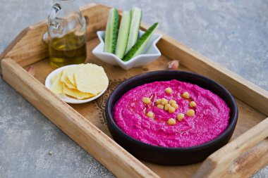 Sağlıklı yiyecekler, kahverengi bir kasede pancar humusu gri beton arka planda tahta bir tepside. Doğranmış sebzelerle servis edilir. Vegan tarifleri.