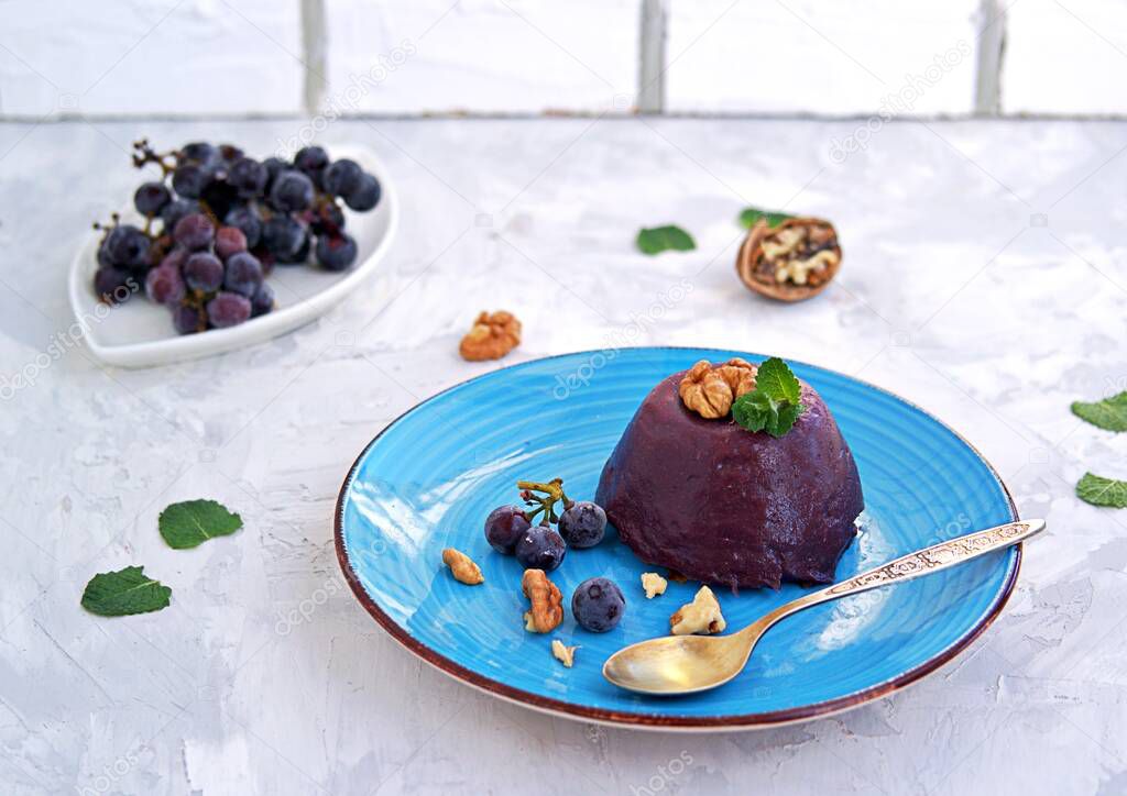 Pelamushi, a Georgian traditional dessert made from grape juice on a blue plate. Decorated with walnuts and berries of frozen grapes. Georgian cuisine.