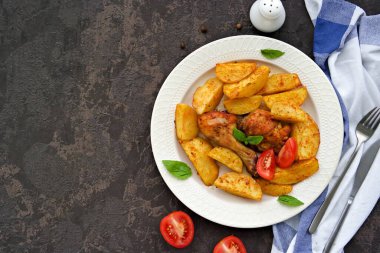 Koyu beton arka planda açık seramik tabakta patates dilimleri ile pişirilmiş but ve tavuk bacağı. Patatesli tarifler. Şükran Günü Tarifleri