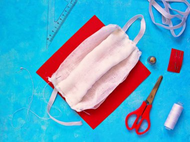 Mavi beton arka planda koruyucu bir tıbbi gazlı bez maskesinin adım adım dikilmesi. Üçüncü adım, kenarları çimdiklemek ve elastik dikiş dikmek. Coronavirus COVID-19 kavramının yayılmasını durdur