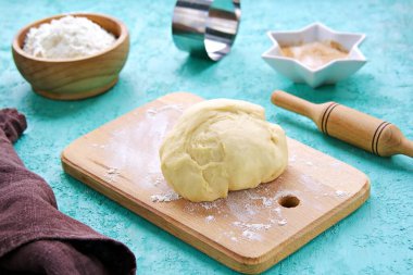 Mutfak arka planı, turkuaz beton bir zeminde pişirmeye ayarlı: pişmiş hamur, ahşap tahta, merdane, un kaplı kase, şeker kaplı yıldız şeklinde kase.