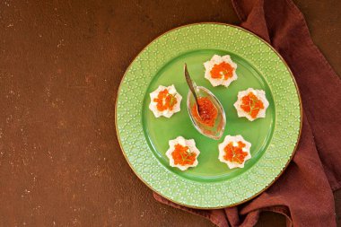 Mini sandviçleri beyaz ekmeğin üzerinde yeşil tabakta kırmızı havyarla kahverengi beton arka planda aç. Abur cubur tarifleri. Sandviç Tarifleri