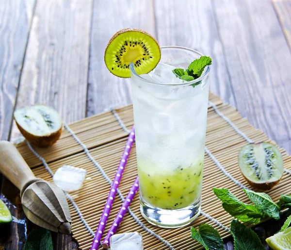 Soft drink, non-alcoholic cocktail with kiwi, lime juice, sparkling water and ice in a tall glass on a wooden background. Non-alcoholic cocktails recipe.
