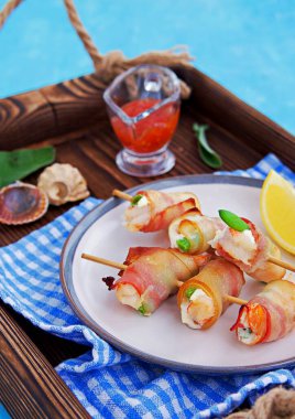 Sıcak aperatif, krem peynirli karides ve kuşkonmaz fasulyesi, pastırmaya sarılmış, seramik tabakta şiş şiş. Deniz ürünleri tarifleri. Atıştırmalık tarifleri.