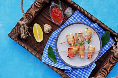 Sıcak aperatif, krem peynirli karides ve kuşkonmaz fasulyesi, pastırmaya sarılmış, seramik tabakta şiş şiş. Deniz ürünleri tarifleri. Atıştırmalık tarifleri.