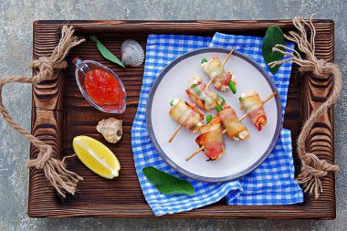 Sıcak aperatif, krem peynirli karides ve kuşkonmaz fasulyesi, pastırmaya sarılmış, seramik tabakta şiş şiş. Deniz ürünleri tarifleri. Atıştırmalık tarifleri.