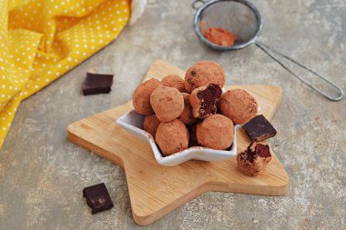 Yıldız şeklinde bir tabakta, gri beton arka planda, tahta bir tahtanın üzerinde ev yapımı çikolatalı şekerler. Yer mantarı şekeri tarifleri. Çikolatalı şekerler. Sevgililer Günü.