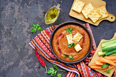 Aperatif humus kırmızı mercimek ve koyu beton arka planda kil kasede kırmızı biber. Tuzlu kraker ve doğranmış sebzelerle servis edilir. Kopyalama alanı.