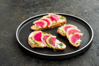 Hafif kahvaltı ya da atıştırmalık, krem peynirli tam tahıllı sandviç, siyah bir tabakta dereotu ve karpuz turpu dilimleri ve koyu beton bir arka plan. Sandviç tarifleri. Sağlıklı yemek.