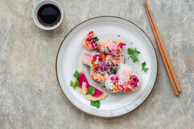 Gri beton arka planda kil bir tabakta karpuz turpu, pirinç eriştesi, havuç ve karidesli parlak bahar börekleri. Asya yemekleri. Sağlıklı yemek..