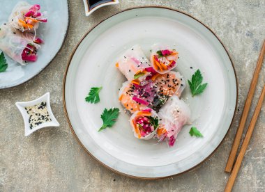 Gri beton arka planda kil bir tabakta karpuz turpu, pirinç eriştesi, havuç ve karidesli parlak bahar börekleri. Asya yemekleri. Sağlıklı yemek..