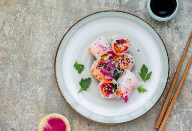 Gri beton arka planda kil bir tabakta karpuz turpu, pirinç eriştesi, havuç ve karidesli parlak bahar börekleri. Asya yemekleri. Sağlıklı yemek..