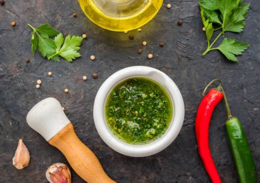 Chimichuri, taze maydanozlu, sarımsaklı, zeytinyağlı ve kekik soslu biftekler için Arjantin yeşil sosu. Tahta bir tahtanın üzerinde koyu beton bir zeminde beyaz bir havan topu. Sos tarifleri. Arjantin mutfağı