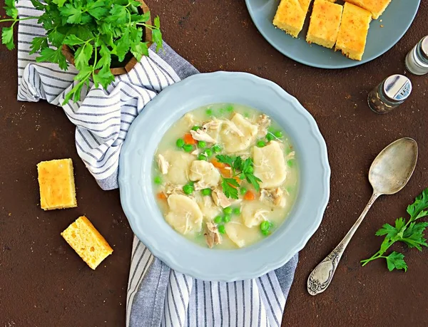 Traditional dish of the American South, dumplings and chicken, green peas in a gray ceramic plate on a brown concrete background. Family meals. American food. Served with cornbread