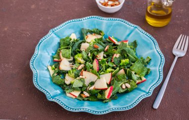 Kahverengi beton arka planda mavi bir tabakta lahana, elma ve badem içeren sağlıklı bir salata. Kale tarifleri. Sağlıklı beslenme