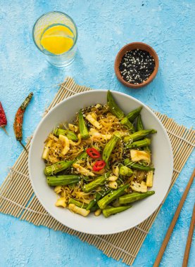 Kızartma, açık mavi beton arka planda gri bir tabakta mürekkep balığı ve bamyayla ince pirinç eriştesi. Bamya tarifleri. Asya yemekleri