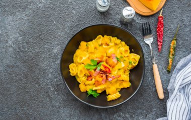 Balkabaklı makarna, kızarmış pastırma ve koyu beton arka planda siyah tabakta acı biber. Makarna tarifleri. İtalyan yemeği..