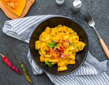 Balkabaklı makarna, kızarmış pastırma ve koyu beton arka planda siyah tabakta acı biber. Makarna tarifleri. İtalyan yemeği..