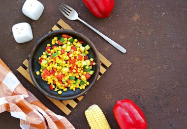 Sebze yahnisi ya da tatlı mısırdan yapılan sıcak salata, kabak ve kırmızı dolma biber kahverengi beton bir arka planda kil tabakta. Vejetaryen tarifleri. Şükran Günü.