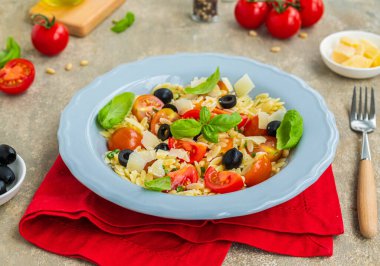 Makarnalı salata, domates, zeytin ve gri beton kaplama gri bir tabakta parmesan. Makarna salatası tarifleri. İtalyan yemeği..