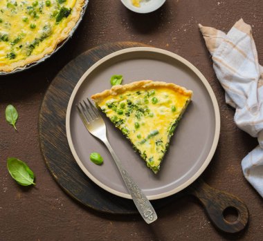 Ispanaklı dilimlenmiş kiş turtası, yeşil bezelye, kuşkonmaz fasulyesi ve kahverengi beton arka planda seramik tabakta yumurta. Fransız mutfağı. Tuzlu hamur işi tarifleri