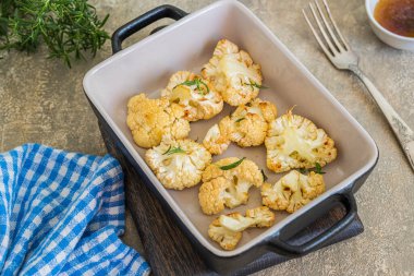 Erimiş kahverengi tereyağlı fırınlanmış karnabahar porsiyonlu bir yemek kabında gri beton arka planda. Vejetaryen tarifleri. Karnabahar Tabakları