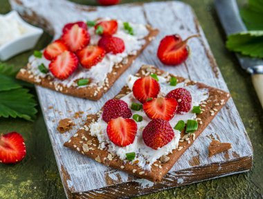 Atıştırmalık veya kahvaltı, krem peynirli çavdar gevreği, yeşil soğan ve yeşil çimento arka planda tahta üzerinde taze çilek. Çilek tarifleri.