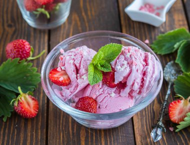 Kahverengi ahşap arka planda şeffaf bir kasede taze çilekli üç kepçe ev yapımı çilekli dondurma. Ev yapımı dondurma tarifleri.