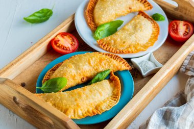 Cheburekler ya da börekler, hafif beton arka planda ahşap tepside kızartılmış geleneksel etli turtalar. Kızarmış hamur işleri..