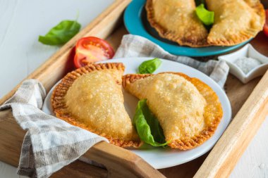 Cheburekler ya da börekler, hafif beton arka planda ahşap tepside kızartılmış geleneksel etli turtalar. Kızarmış hamur işleri..