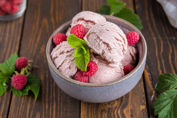 Balls of raspberry ice cream with fresh raspberries in a ceramic bowl on a brown wooden background. Ice cream recipes. Summer concept