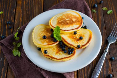 Kahverengi ahşap zemin üzerinde beyaz bir tabakta mısır unu ve yaban mersinli krepler. Krep tarifleri..