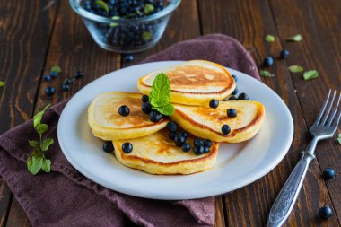 Kahverengi ahşap zemin üzerinde beyaz bir tabakta mısır unu ve yaban mersinli krepler. Krep tarifleri..