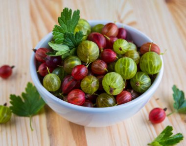 Kırmızı ve yeşil bektaşi üzümleri seramik bir kasede, açık ahşap bir arka planda. Yemek malzemesi. Bektaşi üzümü hasadı