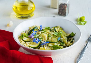 Makarnalı salata, kızarmış kabak ve zeytinyağı soslu sarımsak açık beton arka planda seramik kasede. Orzo salatası. Kabak tarifleri