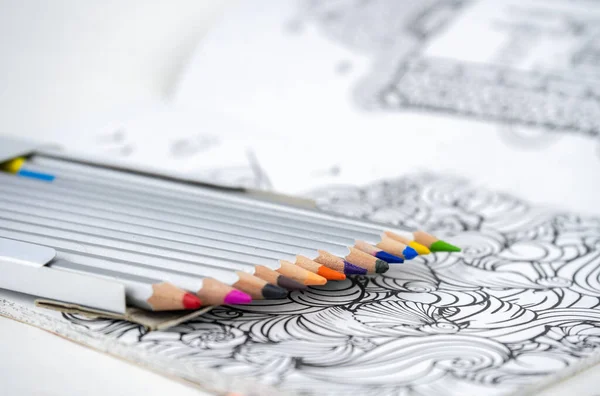 Set of colored pencils in a box and coloring book on a table