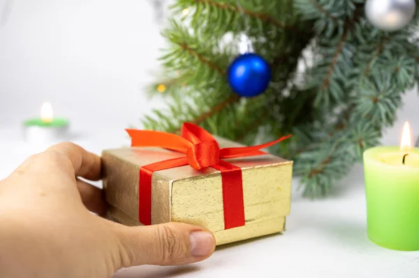 Golden present gift box with red ribbon next to the christmas tree, candles and holiday decoration. Merry Christmas or Happy New Year greeting card. White background