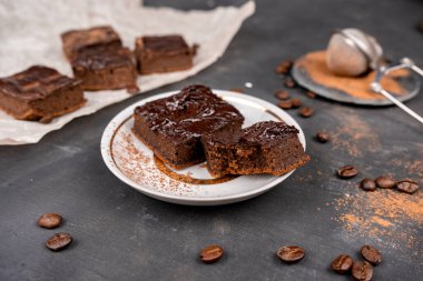 Kakaolu browniler erimiş siyah çikolatayla beyaz bir tabakta kare şeklinde kesilmiş. Siyah arkaplan.