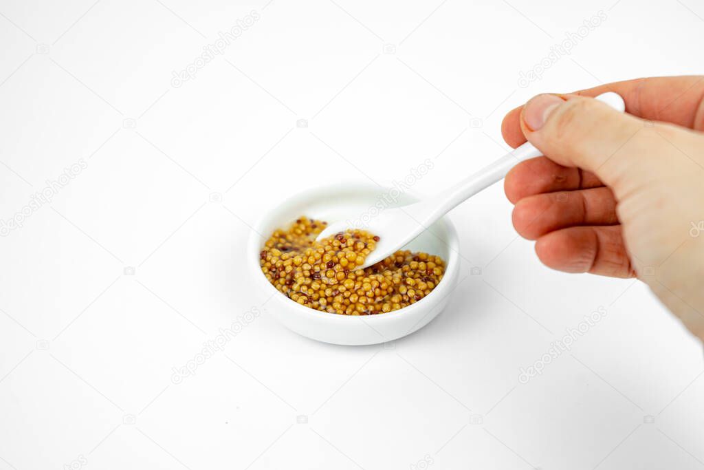 granular seeded dijon mustard in a small plate with little spoon. Isolated on white