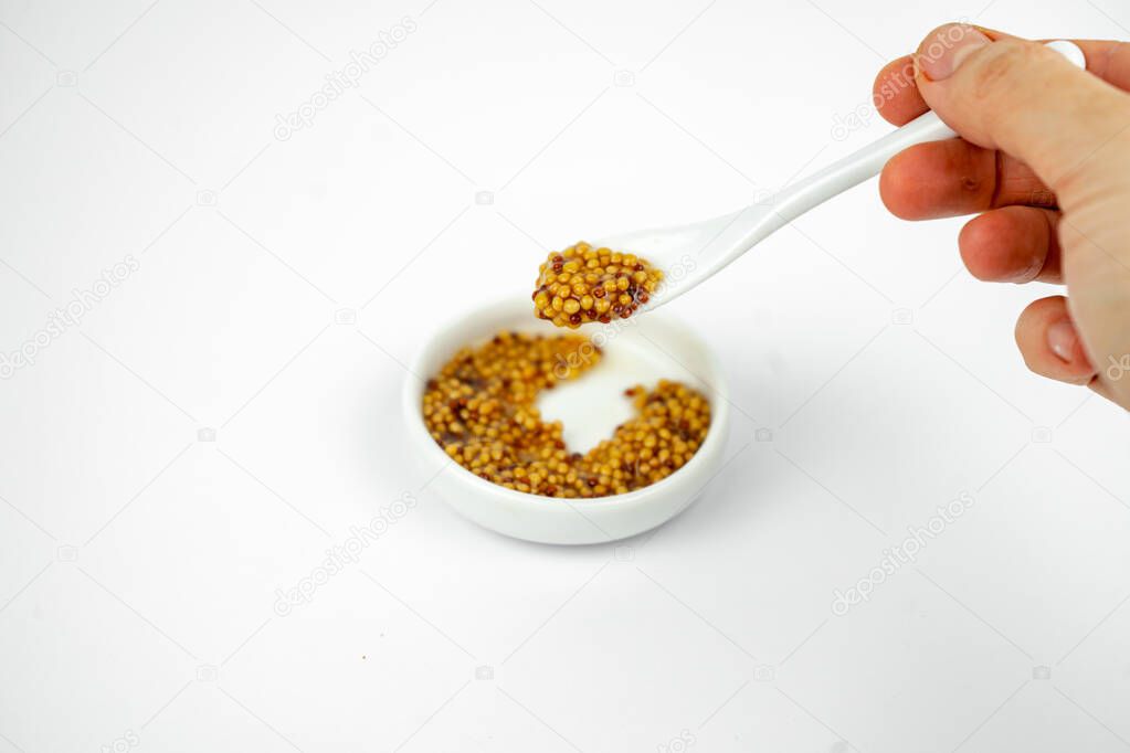 granular seeded dijon mustard in a small plate with little spoon. Isolated on white