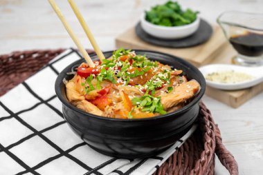 Pirinç erişteli Asya salatası, sebze, mantar, tavuk ve soya sosu. Siyah tabakta beyaz şeffaf şehriye.