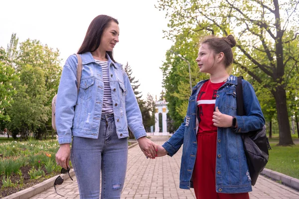 Anne ve genç kız parkta el ele tutuşuyorlar, uzun saçlı mutlu beyaz kadın ve genç kız şehirde takılıyor, yaşam tarzı aile.