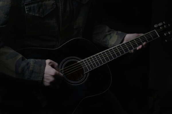 Low-key photo of the hands of a musician with a black guitar, against a dark background. guitar music photo aesthetics