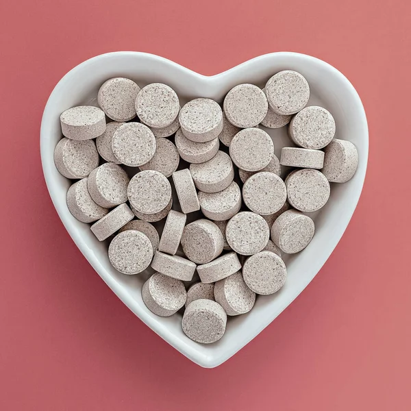 close-up of DGL (licorice root extract) chewable tablets. dietary concept: white porcelain heart-shaped bowl full of DGL pills. food supplement topview