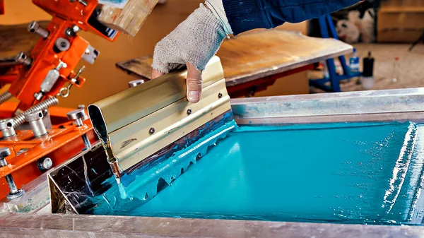 Parmak izi tarama cihazı ve bir işçinin seçici odak fotoğrafı. serigrafi üretimi. Bir tasarım stüdyosunda ipek ekran yöntemiyle tişörtlere resimler basmak