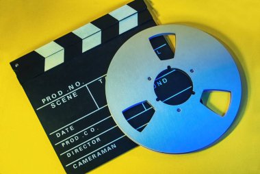 Bir film tahtası ve sarı arka planda bir bant makarasının tam kare fotoğrafı. Sinema, film konsepti.