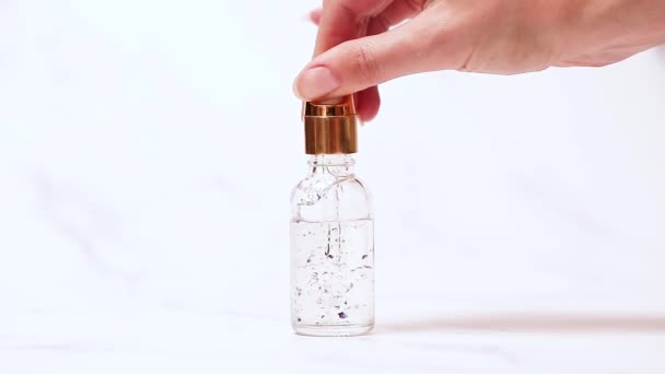 Bouteille d'huile cosmétique soin de la peau sur fond de marbre clair. La main des filles tient une pipette et goutte de l'huile. enzymes bénéfiques et vitamines du squalène, de l'eau de fleur et du sérum cosmétique. — Video