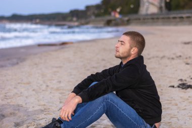 Genç adam akşamları deniz kıyısında oturup suya bakıyor. Romantik ruh hali, seçici odaklanma.