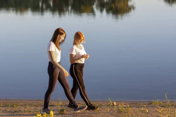 Two young friends are walking along the river bank. Friendship and love concept. Soft focus, blur.
