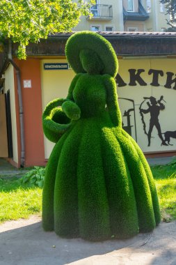 Pionersky, Kaliningrad Bölgesi, Rusya - Eylül 2020: Uzun elbiseli ve yeşil çimenden yapılmış şapkalı kadın çalı figürü. Şehir bitkisi..